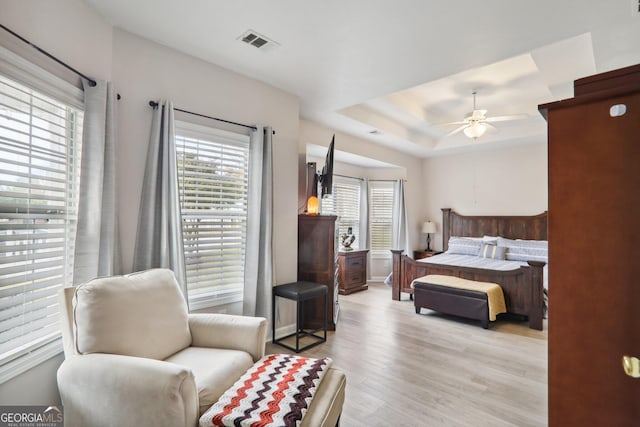 bedroom with light hardwood / wood-style floors, ceiling fan, multiple windows, and a raised ceiling