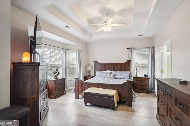 bedroom with light wood-type flooring, a tray ceiling, and ceiling fan