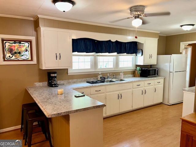 kitchen with kitchen peninsula, ornamental molding, a kitchen breakfast bar, white cabinets, and white fridge