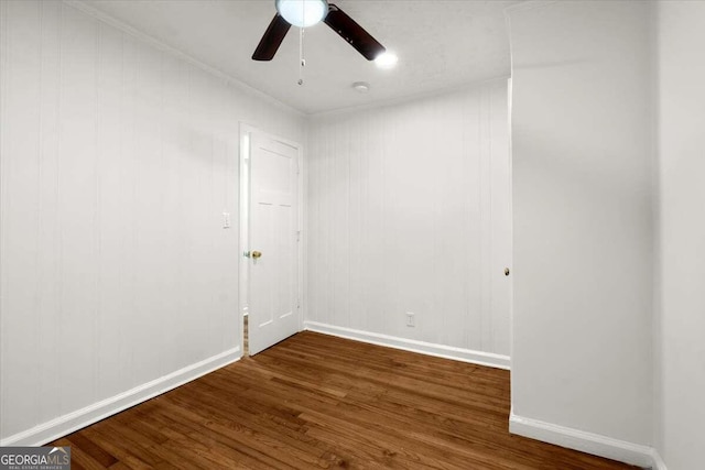 empty room with dark hardwood / wood-style flooring, wood walls, ceiling fan, and crown molding