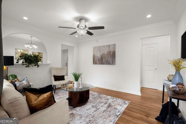 living room featuring wood-type flooring, ornamental molding, and ceiling fan with notable chandelier