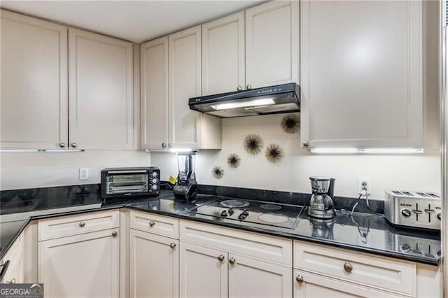 kitchen with dark stone countertops, white cabinetry, and black stovetop