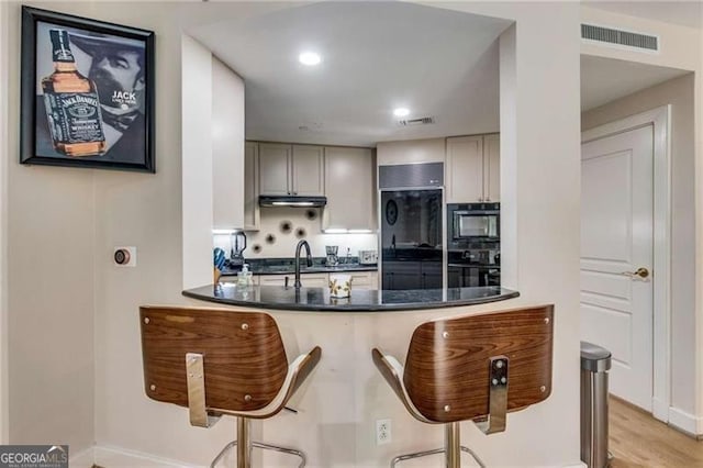 kitchen featuring a breakfast bar, gray cabinets, and black appliances