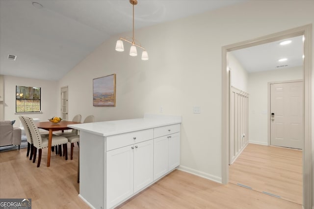 kitchen with kitchen peninsula, light wood-type flooring, vaulted ceiling, white cabinetry, and hanging light fixtures