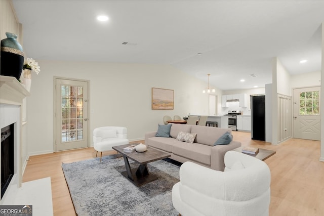 living room with a chandelier, a premium fireplace, light hardwood / wood-style floors, and lofted ceiling