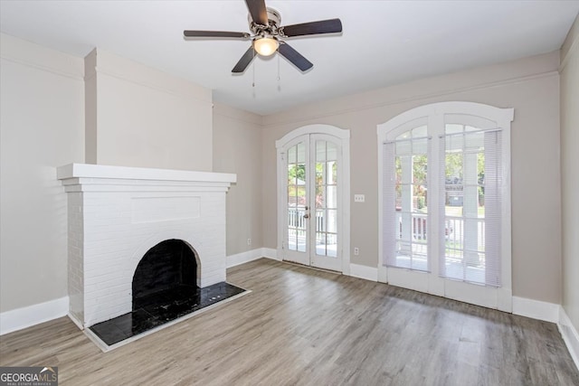 unfurnished living room featuring a brick fireplace, french doors, hardwood / wood-style flooring, and ceiling fan