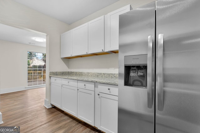 kitchen with white cabinets, stainless steel refrigerator with ice dispenser, light stone counters, and light hardwood / wood-style floors