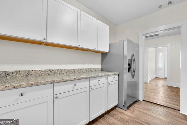 kitchen with light stone countertops, stainless steel fridge, white cabinetry, and light wood-type flooring