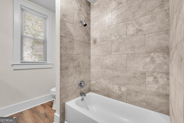 bathroom with wood-type flooring, tiled shower / bath combo, and toilet