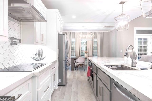 kitchen with wall chimney range hood, hanging light fixtures, decorative backsplash, and white cabinets