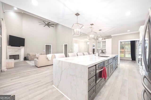 kitchen with pendant lighting, oven, a center island with sink, and light wood-type flooring