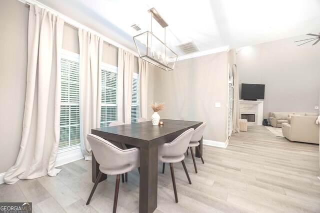 dining area with a fireplace, ceiling fan with notable chandelier, light hardwood / wood-style floors, and plenty of natural light