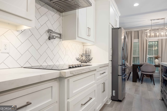 kitchen featuring stainless steel fridge, custom range hood, white cabinets, black electric cooktop, and light hardwood / wood-style flooring