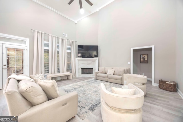 living room featuring ornamental molding, a fireplace, light wood-type flooring, a high ceiling, and ceiling fan