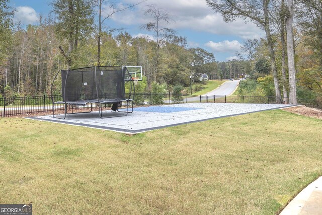 view of basketball court with a trampoline and a lawn