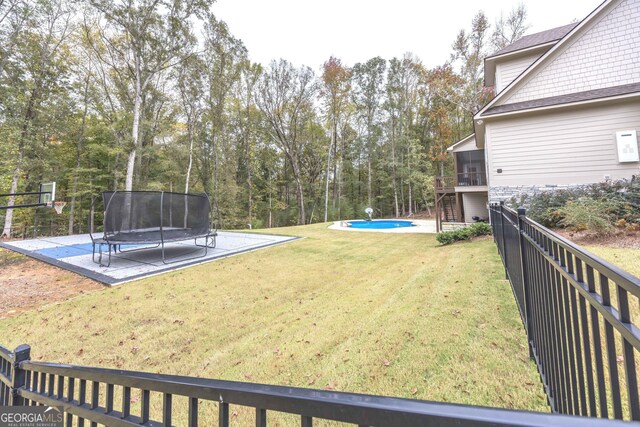 view of yard featuring a sunroom, a trampoline, a fenced in pool, and a patio area