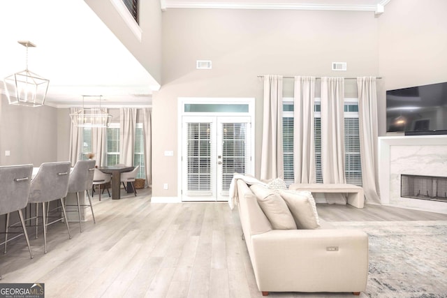 living room featuring light hardwood / wood-style floors, ornamental molding, an inviting chandelier, a high end fireplace, and french doors