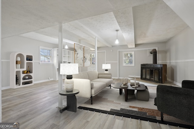 living room featuring wood-type flooring, a wood stove, and beam ceiling