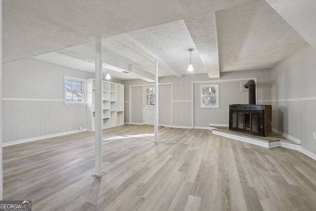 basement featuring a wood stove, a textured ceiling, and light wood-type flooring