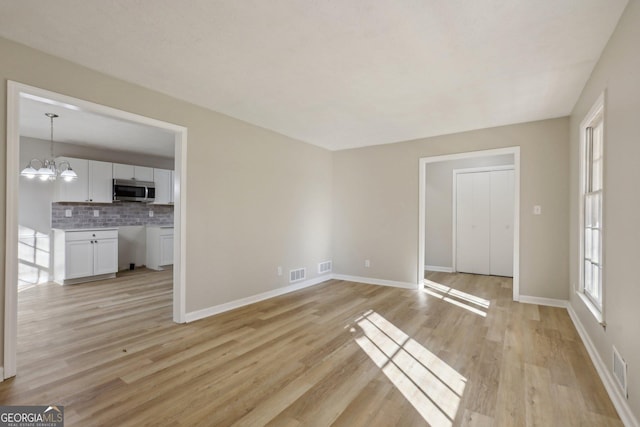 unfurnished living room with a chandelier and light wood-type flooring