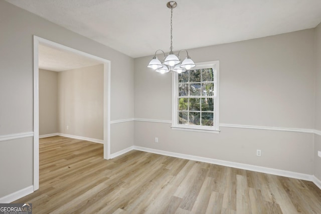 empty room featuring a notable chandelier and light wood-type flooring