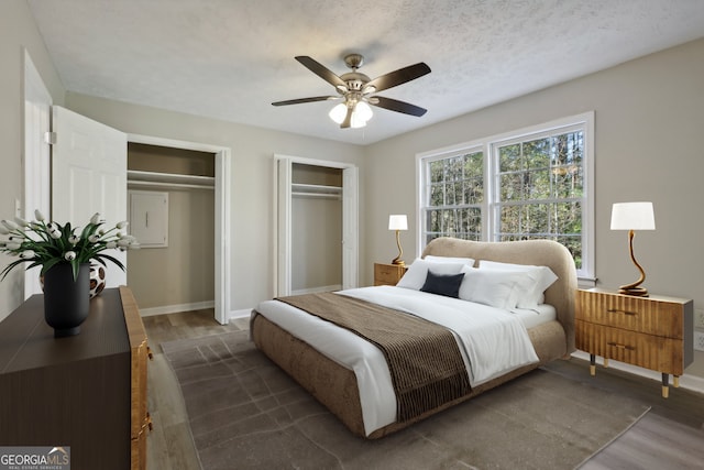 bedroom with a textured ceiling, dark hardwood / wood-style flooring, ceiling fan, and multiple closets