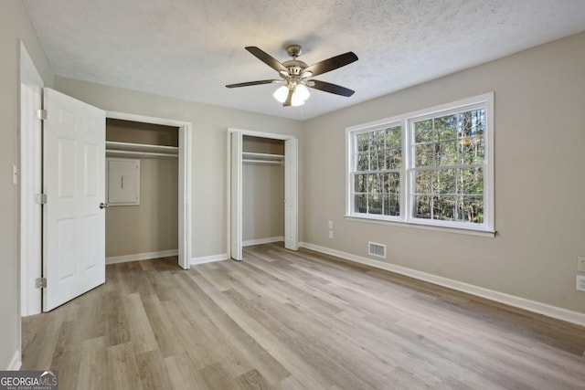 unfurnished bedroom with a textured ceiling, light wood-type flooring, two closets, and ceiling fan