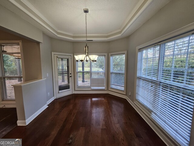 unfurnished dining area featuring ornamental molding, a textured ceiling, a tray ceiling, dark wood-type flooring, and a notable chandelier