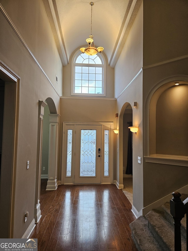 foyer featuring a high ceiling, dark hardwood / wood-style flooring, decorative columns, and a notable chandelier