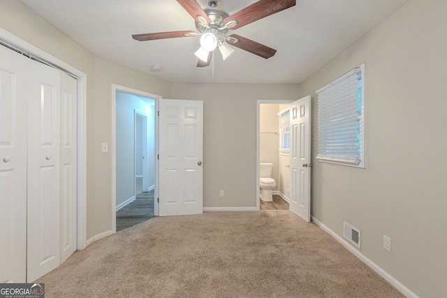 unfurnished bedroom with a closet, light carpet, ceiling fan, and ensuite bath