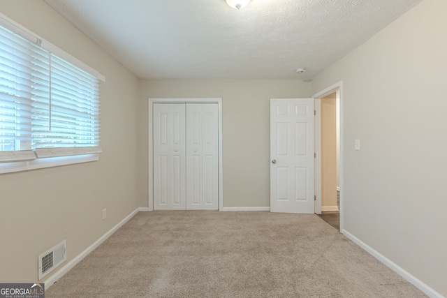 unfurnished bedroom featuring a closet, a textured ceiling, and light carpet