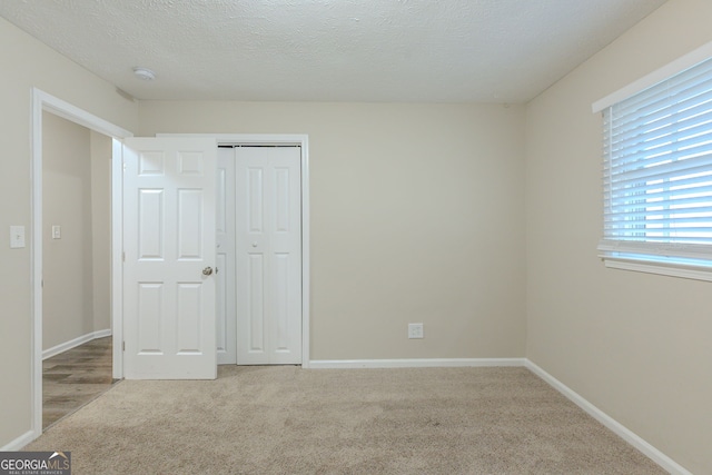 unfurnished bedroom featuring a textured ceiling, light carpet, and a closet