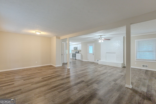 unfurnished living room featuring ceiling fan, hardwood / wood-style flooring, a brick fireplace, and plenty of natural light