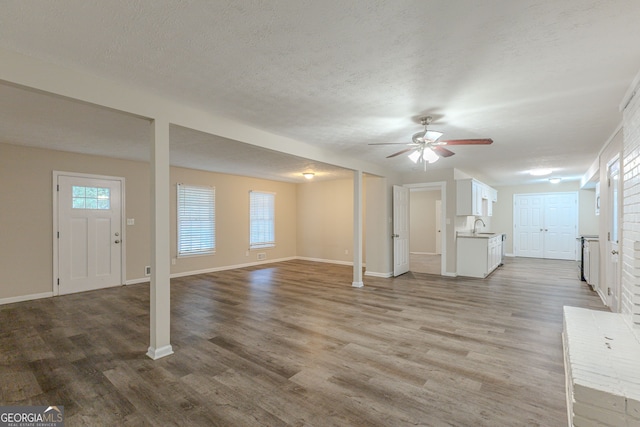 unfurnished living room featuring a textured ceiling, light hardwood / wood-style floors, ceiling fan, and sink