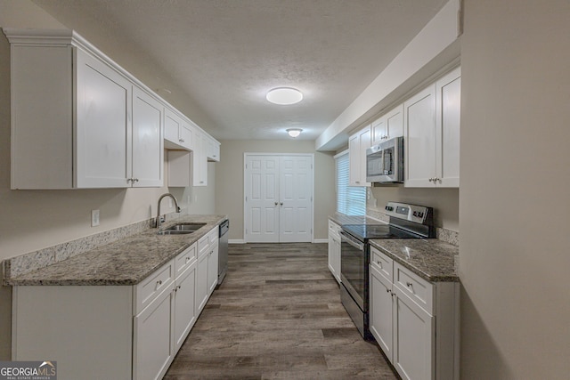 kitchen with white cabinets, sink, light wood-type flooring, appliances with stainless steel finishes, and dark stone countertops