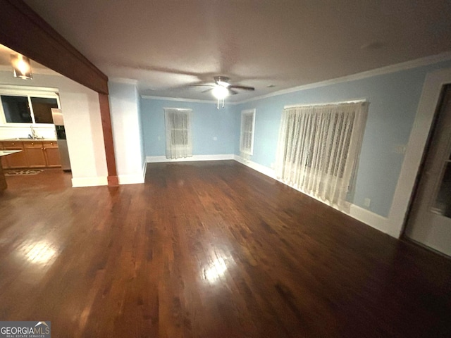 unfurnished living room with sink, dark wood-type flooring, ornamental molding, and ceiling fan