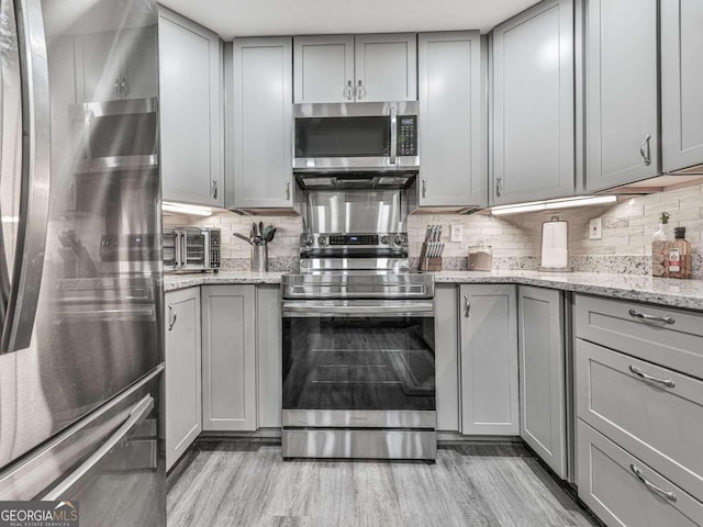 kitchen with gray cabinets, light stone countertops, and appliances with stainless steel finishes