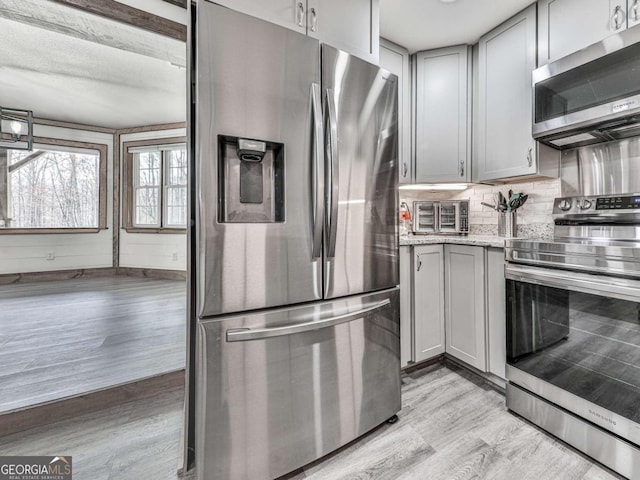 kitchen featuring tasteful backsplash, light stone counters, light wood-type flooring, appliances with stainless steel finishes, and gray cabinets