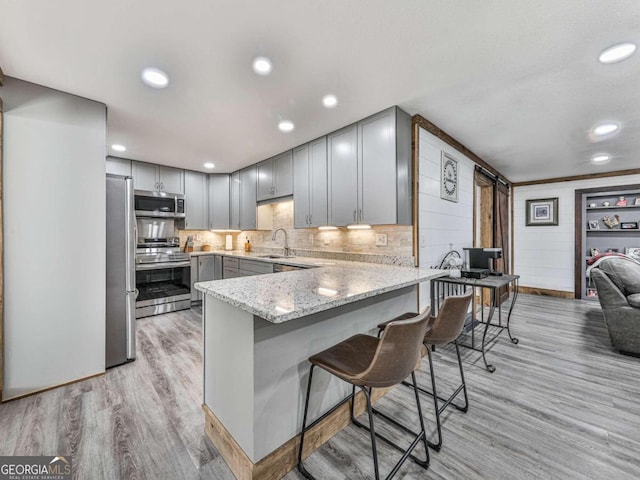 kitchen featuring stainless steel appliances, a kitchen bar, light stone countertops, sink, and light hardwood / wood-style flooring