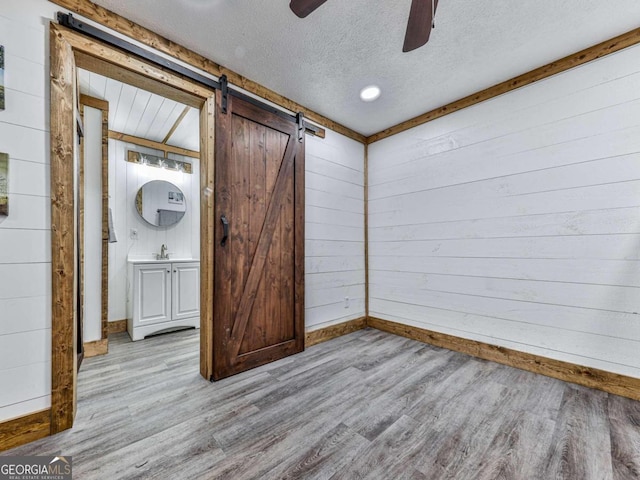 interior space featuring ceiling fan, a textured ceiling, light hardwood / wood-style flooring, a barn door, and wooden walls