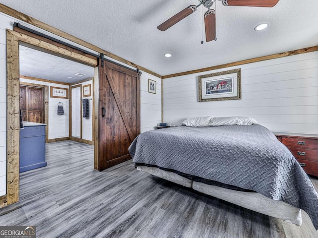 bedroom with a textured ceiling, a barn door, ceiling fan, and wood-type flooring