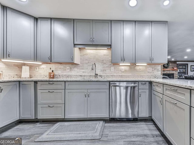 kitchen featuring light wood-type flooring, gray cabinets, light stone countertops, sink, and stainless steel dishwasher