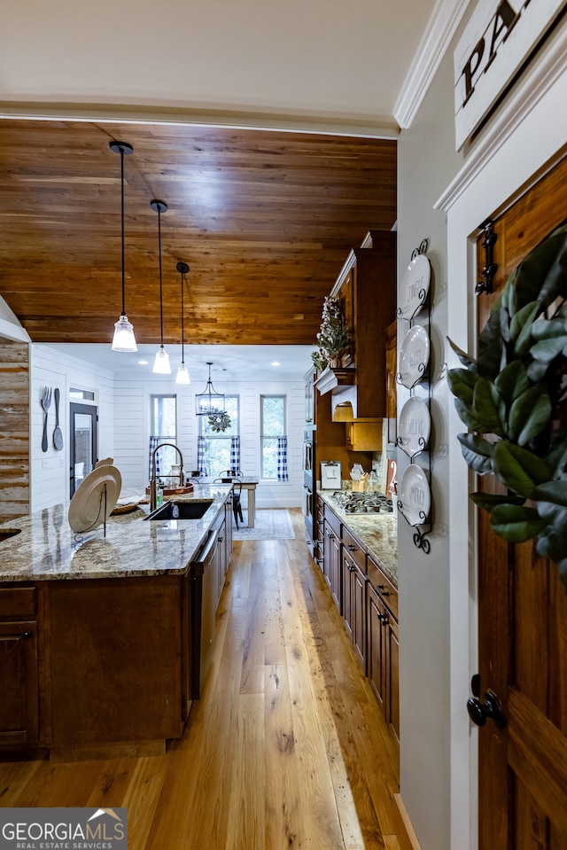 kitchen featuring light stone counters, ornamental molding, hanging light fixtures, sink, and light hardwood / wood-style flooring