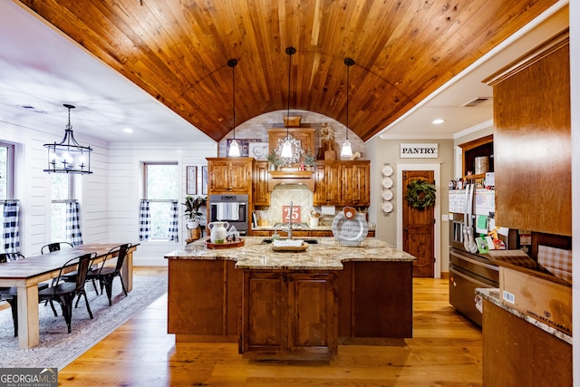 kitchen with pendant lighting, an island with sink, light stone countertops, and light wood-type flooring