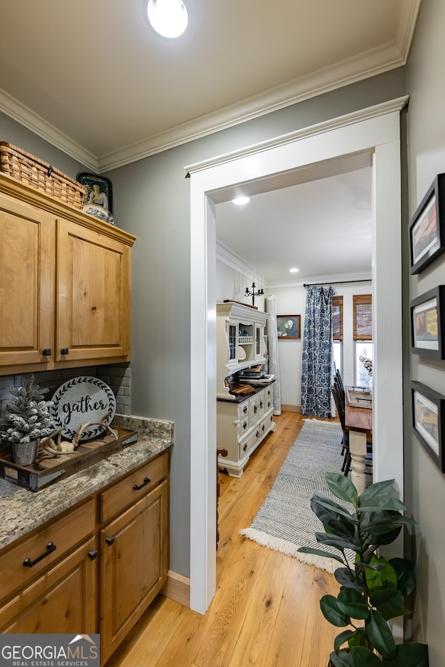 kitchen with tasteful backsplash, light stone counters, ornamental molding, and light hardwood / wood-style flooring