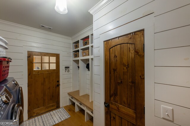 mudroom with light wood-type flooring, wooden walls, crown molding, and washer and dryer