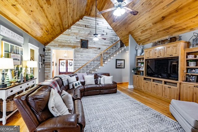 living room with wood walls, light hardwood / wood-style floors, ceiling fan, and high vaulted ceiling