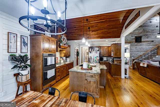 kitchen with light wood-type flooring, an inviting chandelier, hanging light fixtures, and a kitchen island with sink