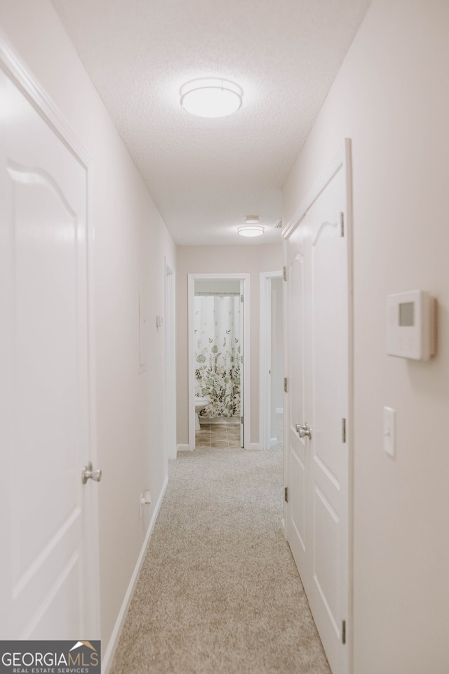 corridor featuring light colored carpet and a textured ceiling