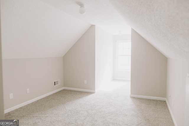 additional living space featuring lofted ceiling, a textured ceiling, and light carpet